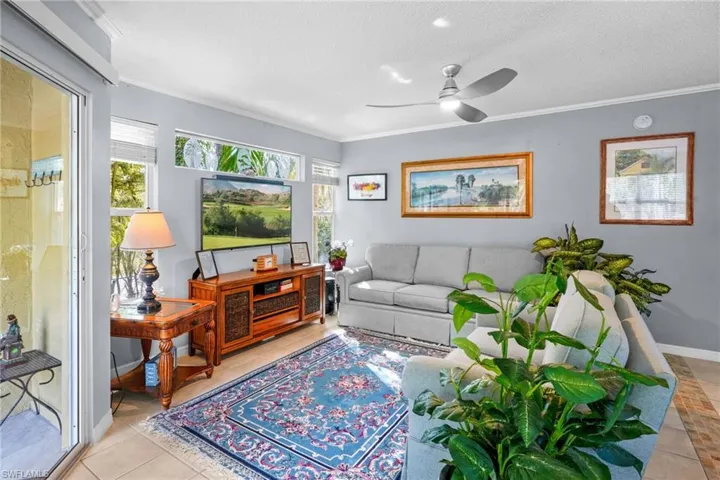 Living room featuring a textured ceiling, ornamental molding, ceiling fan, and light tile patterned floors