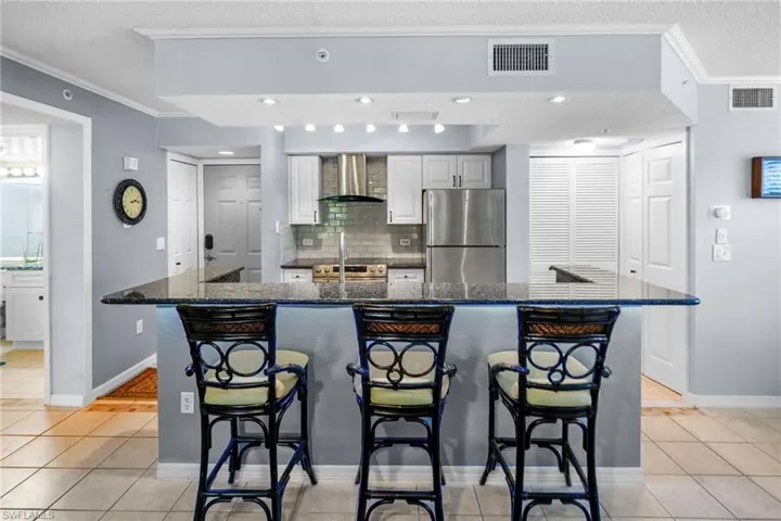 Kitchen with a kitchen bar, light tile patterned flooring, dark stone counters, crown molding, and freestanding refrigerator