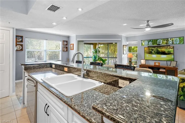 Kitchen with light tile patterned floors, a textured ceiling, white cabinetry, dark stone counters, and a kitchen island with sink