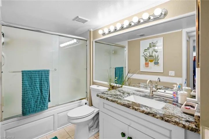 Bathroom featuring enclosed tub / shower combo, vanity, and light tile patterned floors