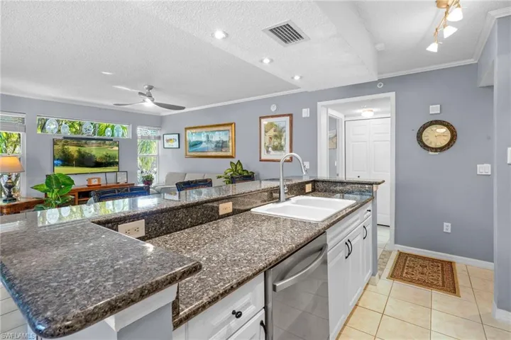 Kitchen featuring white cabinets, stainless steel dishwasher, light tile patterned floors, dark stone counters, and ceiling fan