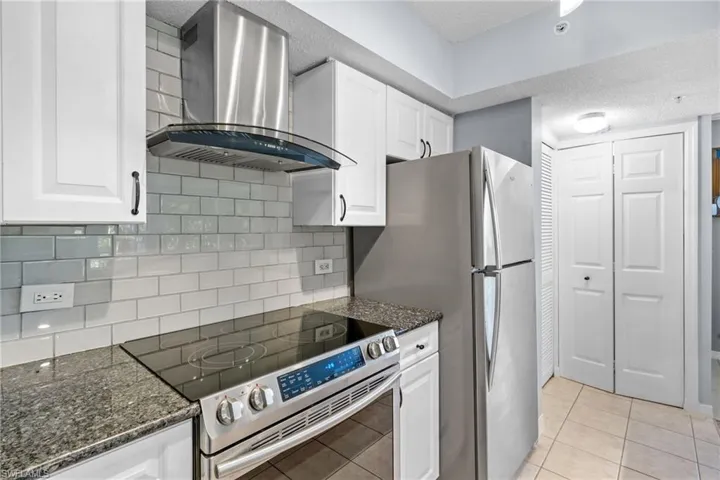 Kitchen featuring stainless steel range with electric cooktop, extractor fan, white cabinetry, dark stone counters, and a textured ceiling