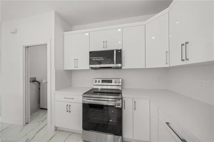 Kitchen featuring white cabinetry, pendant lighting, light marble finish flooring, appliances with stainless steel finishes, and a large island with sink