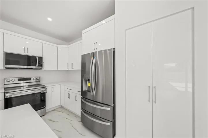 Kitchen with white cabinetry, light marble finish floors, appliances with stainless steel finishes, an island with sink, and pendant lighting
