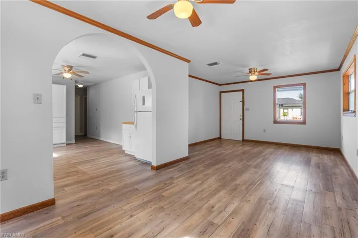Unfurnished living room with ceiling fan, arched walkways, ornamental molding, and light wood finished floors