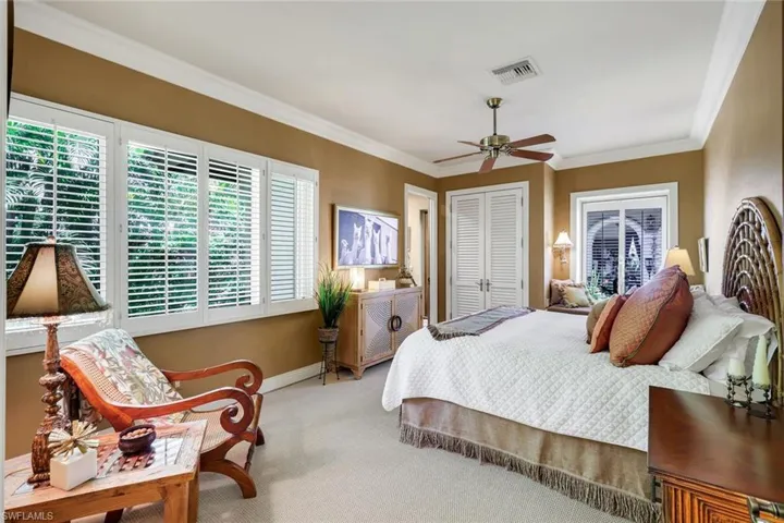 Spacious bedroom featuring light-colored carpet flooring, crown molding, and a ceiling fan