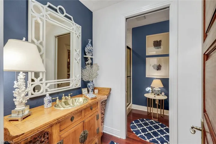 Vanity area featuring a brass vessel sink set in a carved wood cabinet, a decorative white mirror, and a deep blue accent wall