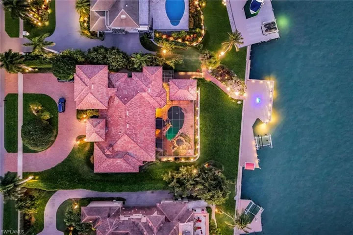 Spacious property featuring a multi-gabled tile roof, a custom-shaped swimming pool, expansive waterfront access, a private dock, and manicured landscaping with exterior lighting