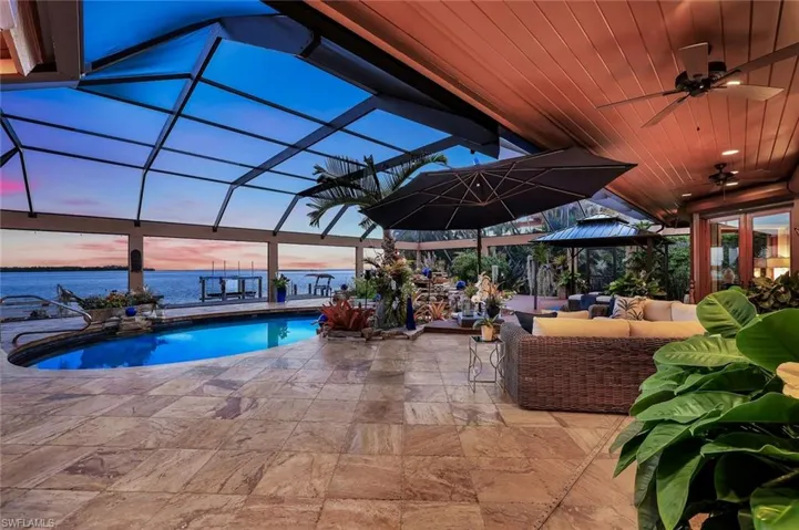 Travertine tile patio featuring a screened enclosure, built-in swimming pool, wood-paneled ceiling, and direct access to the water