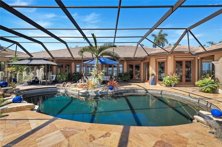 Screen-enclosed pool area featuring a freeform swimming pool, extensive stone paver decking, and a built-in spa with rock accents