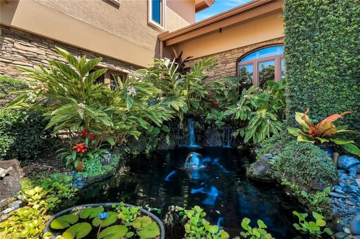 Lush landscaping encompassing a koi pond with a water feature, a small waterfall, and varied tropical plantings