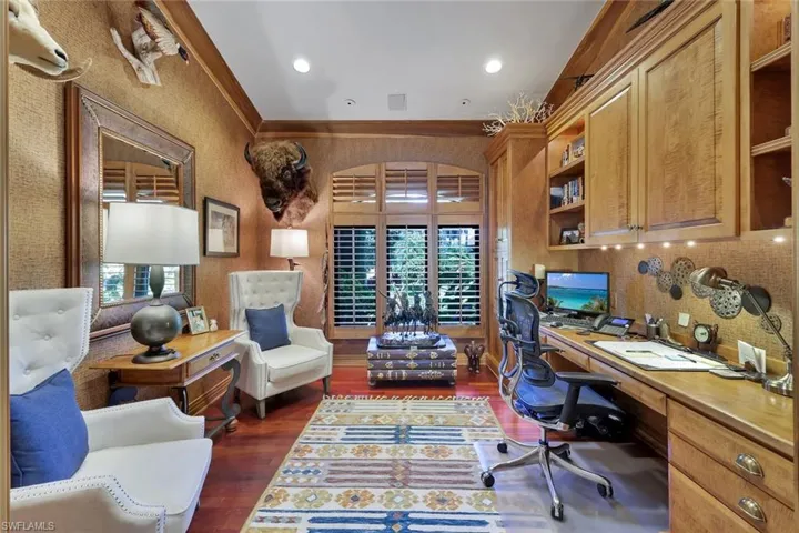 Dedicated office space featuring extensive built-in wooden cabinetry, recessed lighting, wood-finish flooring, and arched windows with plantation shutters
