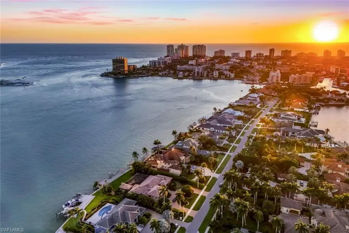 Aerial perspective showcasing waterfront properties with private docks, a palm-lined street, multiple residential structures, and distant high-rise buildings