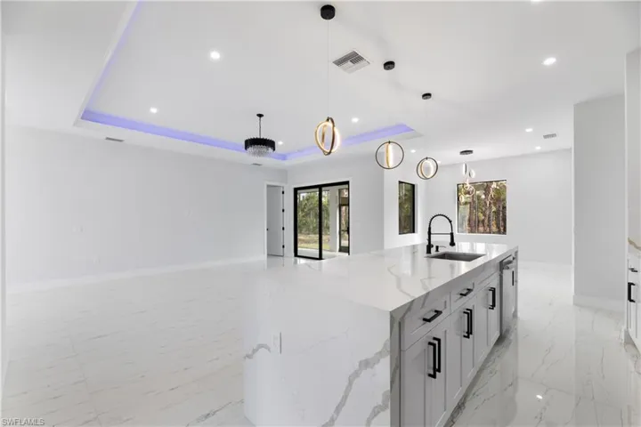 Kitchen with a raised ceiling, a sink, a large island with sink, and pendant lighting