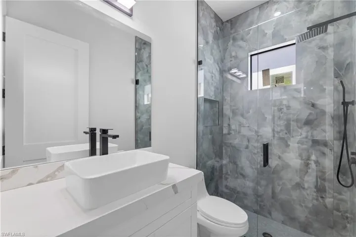 Bathroom with toilet, a marble finish shower, and vanity