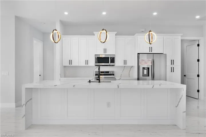 Kitchen with stainless steel appliances, light stone counters, and a spacious island