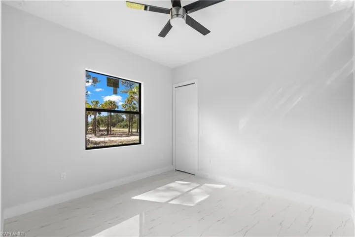 Empty room featuring marble finish floor, ceiling fan, and baseboards