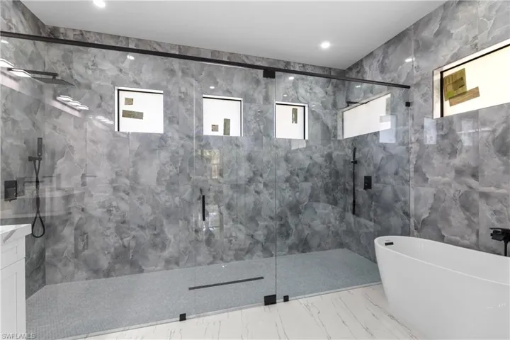 Full bath featuring marble finish floor, a marble finish shower, tile walls, and a soaking tub