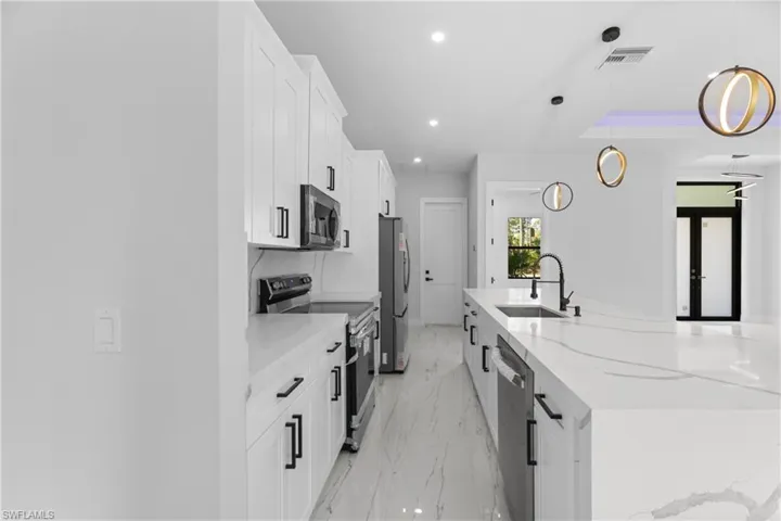 Kitchen featuring visible vents, appliances with stainless steel finishes, white cabinetry, pendant lighting, and a sink