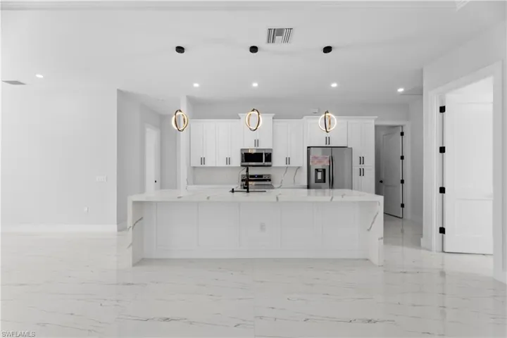 Kitchen with white cabinets, stainless steel appliances, a large island with sink, and decorative light fixtures