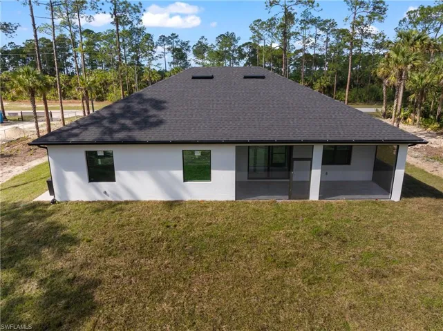 Rear view of property featuring a shingled roof, a lawn, and stucco siding