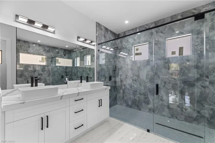 Bathroom with double vanity, marble finish floor, a sink, and a stall shower