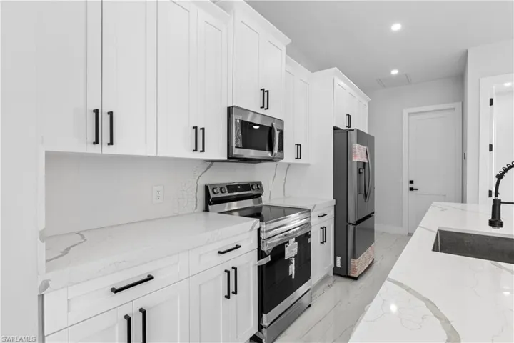 Kitchen with marble finish floor, stainless steel appliances, white cabinetry, a sink, and light stone countertops