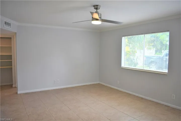 Empty room featuring a ceiling fan, ornamental molding, baseboards, and visible vents