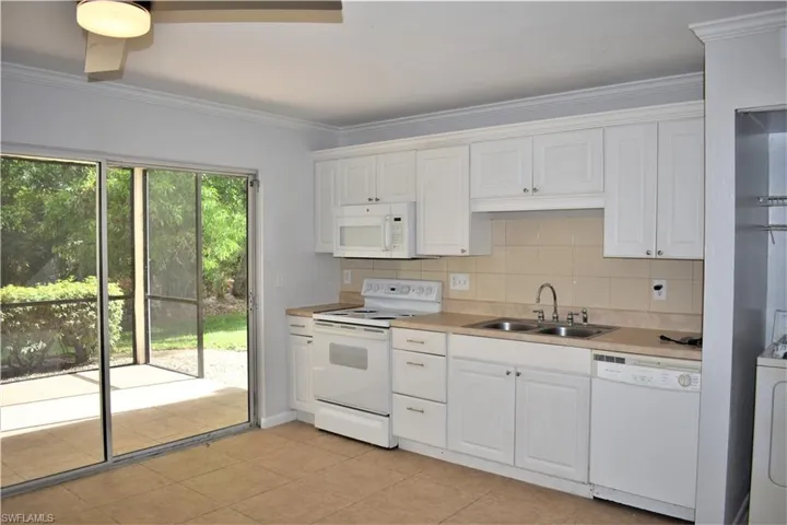 Kitchen with white appliances, white cabinetry, tasteful backsplash, and a sink