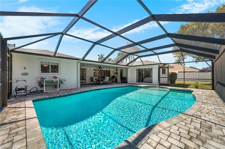 View of pool featuring a covered lanai with ceiling fan & sliders to dining room, family room, guest bedroom & owners bedroom.