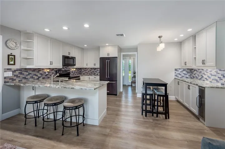 Updated kitchen featuring a peninsula, tasteful backsplash, white cabinetry, open shelves, and newer appliances with stainless steel finishes.