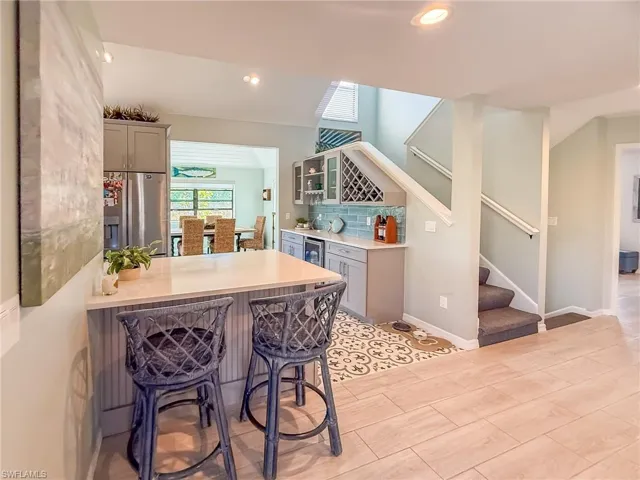 Kitchen featuring gray cabinets, a kitchen breakfast bar, backsplash, stainless steel fridge, and light countertops