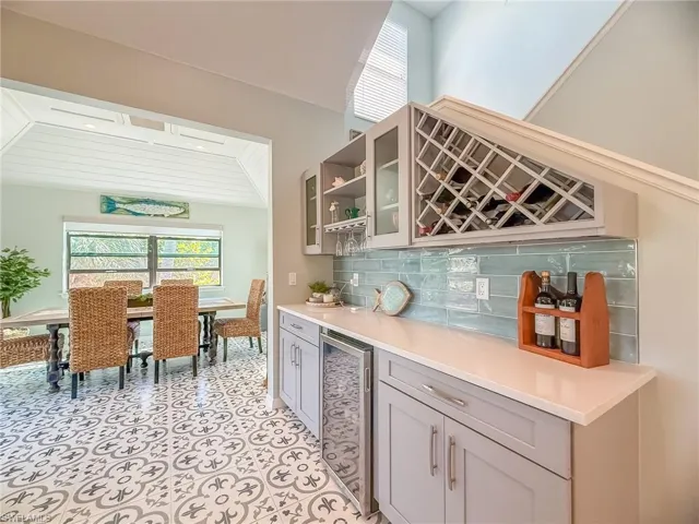 Bar featuring beverage cooler, light tile patterned flooring, a bar, and tasteful backsplash