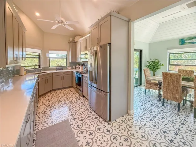 Kitchen with a sink, appliances with stainless steel finishes, light tile patterned floors, ceiling fan, and vaulted ceiling