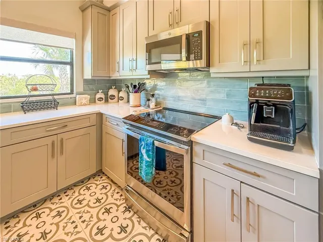Kitchen with light tile patterned flooring, gray cabinets, stainless steel appliances, decorative backsplash, and light countertops