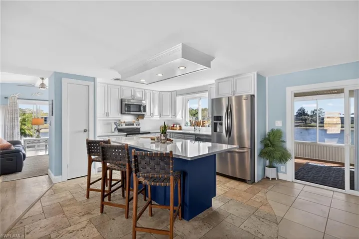 Kitchen with stainless steel appliances, a kitchen island, stone tile flooring, dual tone cabinetry, and a breakfast bar area