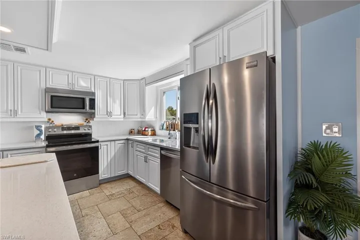 Kitchen featuring stainless steel appliances, stone tile floors, white cabinetry, and light stone counters