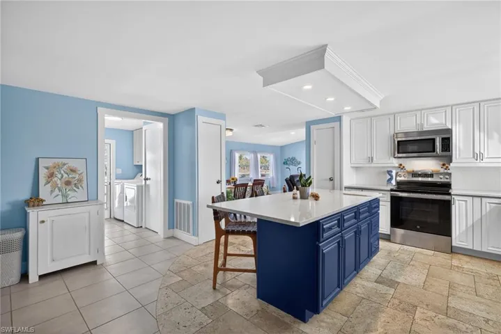 Kitchen featuring two tone cabinetry, stainless steel appliances, a breakfast bar, a center island, and independent washer and dryer