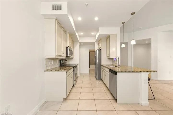 Kitchen with light stone countertops, a breakfast bar area, stainless steel appliances, a peninsula, and pendant lighting
