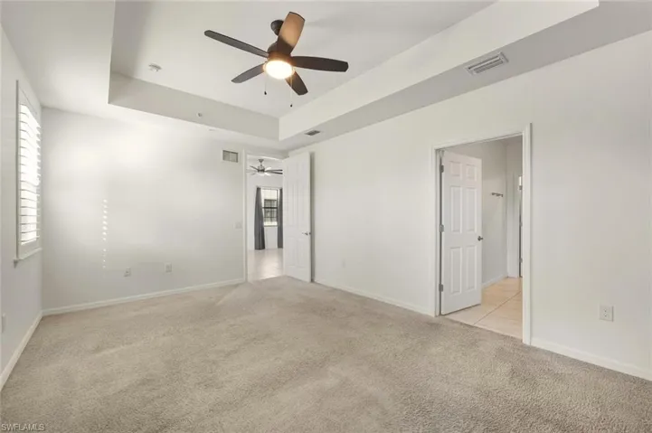 Unfurnished bedroom featuring a raised ceiling, light colored carpet, and ceiling fan