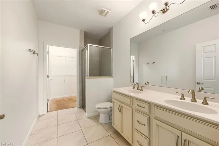Bathroom with a stall shower, double vanity, a spacious closet, and light tile patterned floors