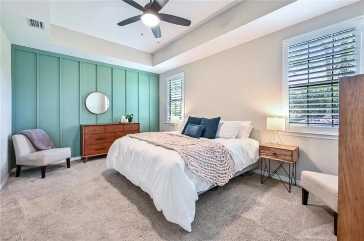 Carpeted bedroom with a raised ceiling, a decorative wall, and a ceiling fan