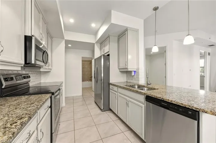 Kitchen with appliances with stainless steel finishes, light stone counters, decorative light fixtures, and tasteful backsplash