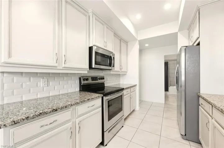 Kitchen featuring appliances with stainless steel finishes, white cabinetry, light stone counters, tasteful backsplash, and light tile patterned flooring