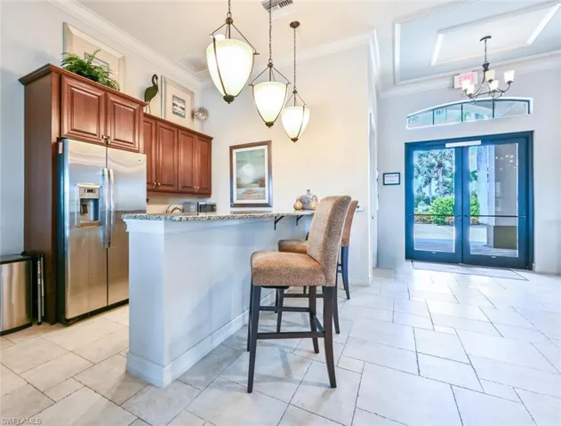 Kitchen featuring stainless steel fridge with ice dispenser, a breakfast bar, hanging light fixtures, light stone countertops, and crown molding
