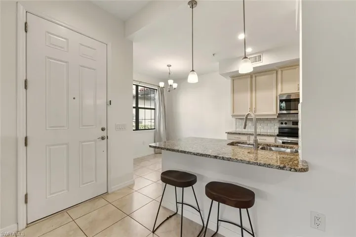 Kitchen with a breakfast bar area, dark stone countertops, tasteful backsplash, decorative light fixtures, and appliances with stainless steel finishes