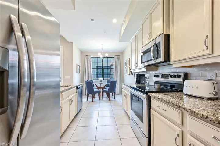 Kitchen with appliances with stainless steel finishes, a chandelier, light tile patterned flooring, light stone countertops, and pendant lighting