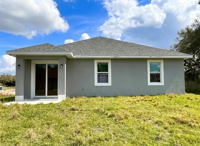 Back of house featuring stucco siding, roof with shingles, and a lawn