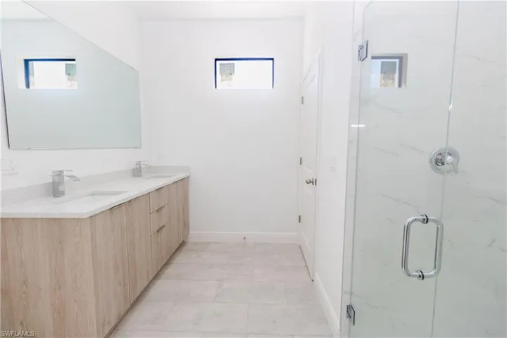 Full bath with double vanity, a marble finish shower, and light tile patterned floors