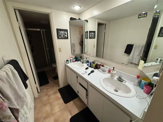 Bathroom with tile flooring, a textured ceiling, double sink, toilet, and oversized vanity